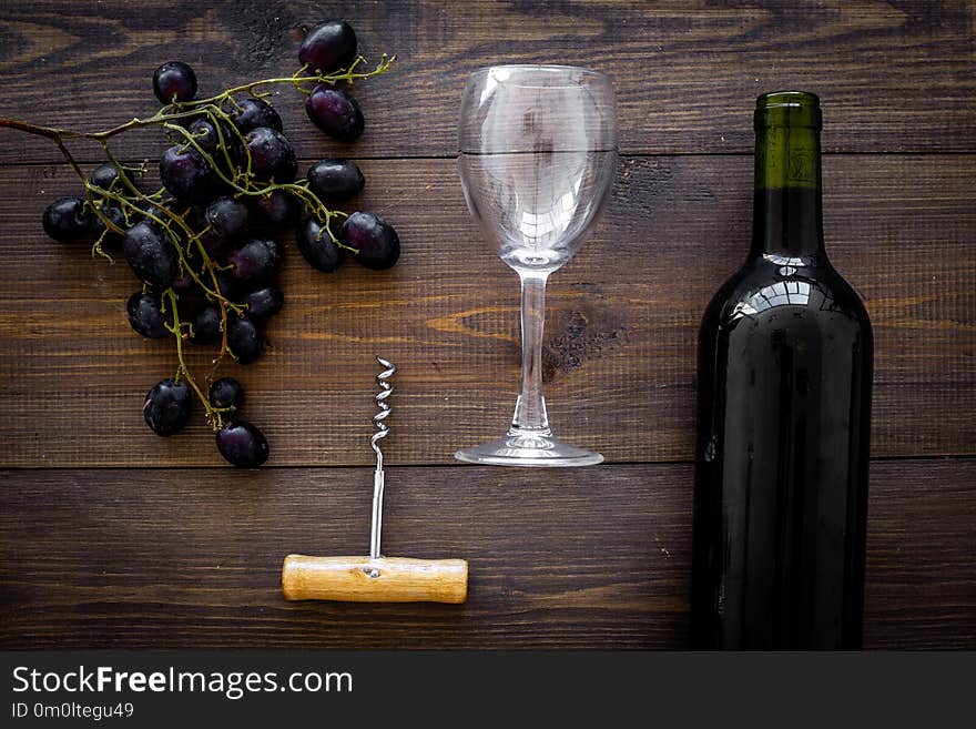 Composition with wine. Red wine bottle, bunch of grapes, corkscrew, wine glass on dark wooden background top view.