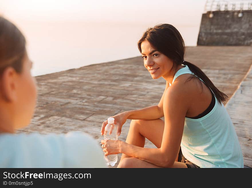 Two sports women friends outdoors on the beach sitting talking with each other