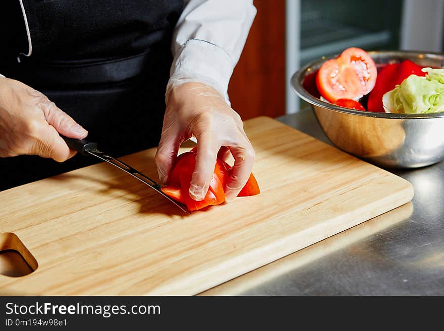 The chef in the cafe cuts tomatoes on a wooden kitchen Board.