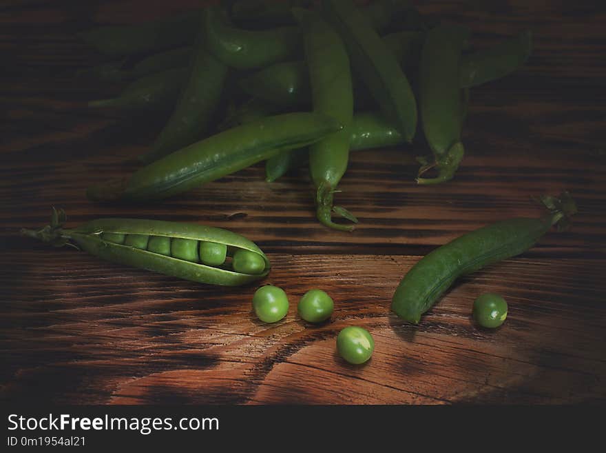 Pods of green peas on the table, a few peas poured out.