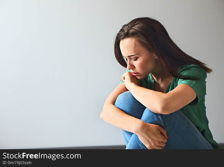 Portrait of a sad woman looking thoughtful about her troubles in front of a gray wall