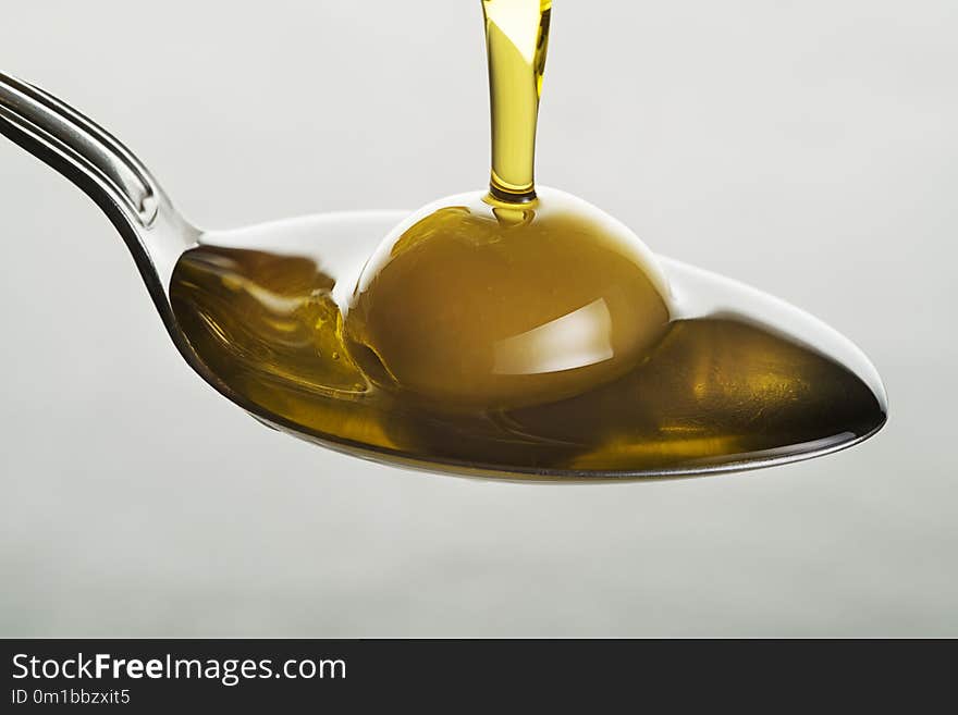 Bottle of virgin olive oil pouring to the spoon close up. Bottle of virgin olive oil pouring to the spoon close up