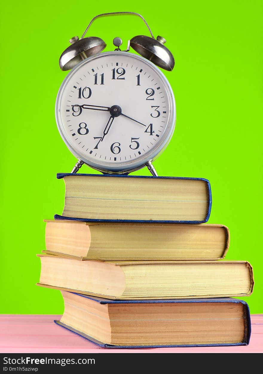 Alarm clock on top of piles of books on yellow background.