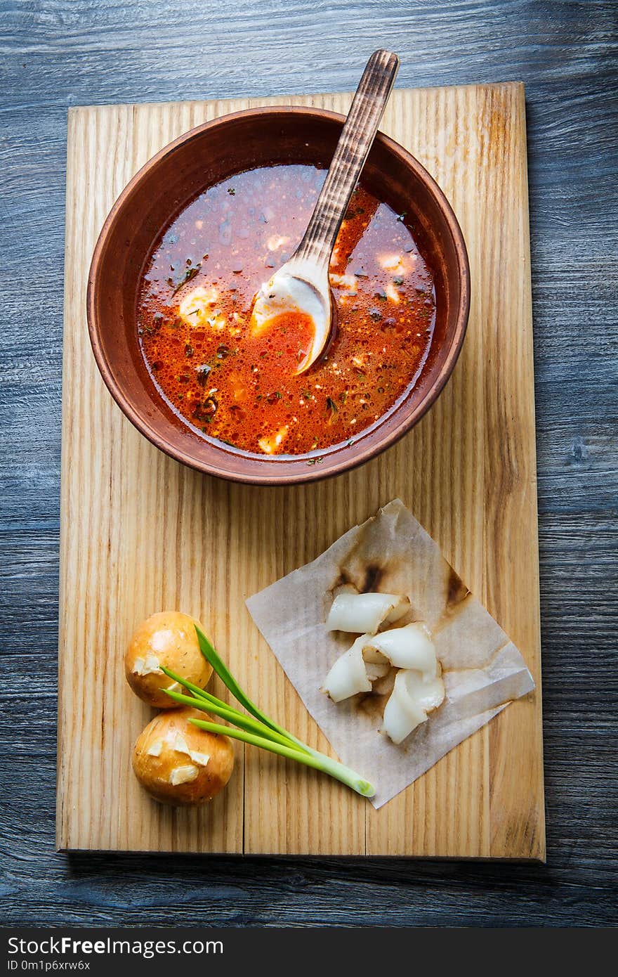 top view on wooden plate with traditional ukrainian borscht next to baked doughnut with garlic topping decorated with green onion and sliced tallow. top view on wooden plate with traditional ukrainian borscht next to baked doughnut with garlic topping decorated with green onion and sliced tallow