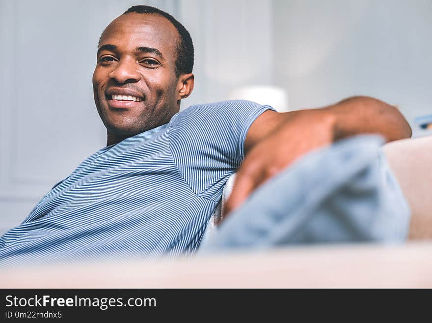 Daily life. Pleasant attractive man looking at you while sitting in a room. Daily life. Pleasant attractive man looking at you while sitting in a room