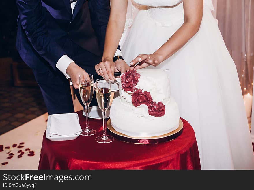 Bride and groom cutting wedding cake and tasting at wedding ceremony reception, catering in restaurant