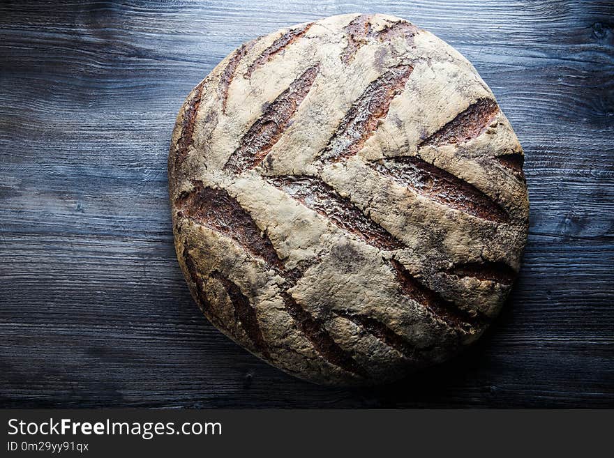 big whole handmade round black bread with interesting texture lie on dark wooden table