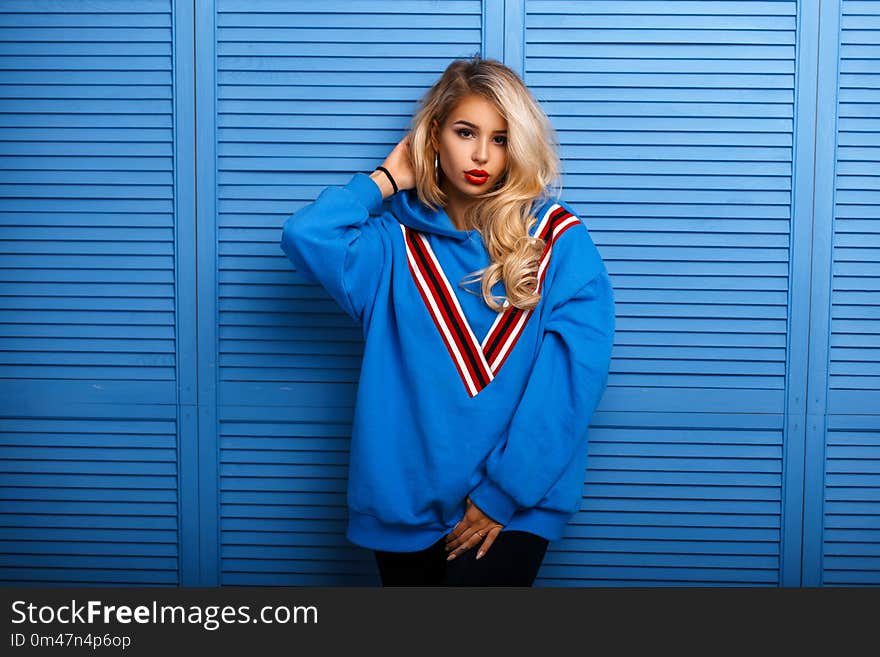 Young stylish woman in blue fashion clothes near a wooden wall.