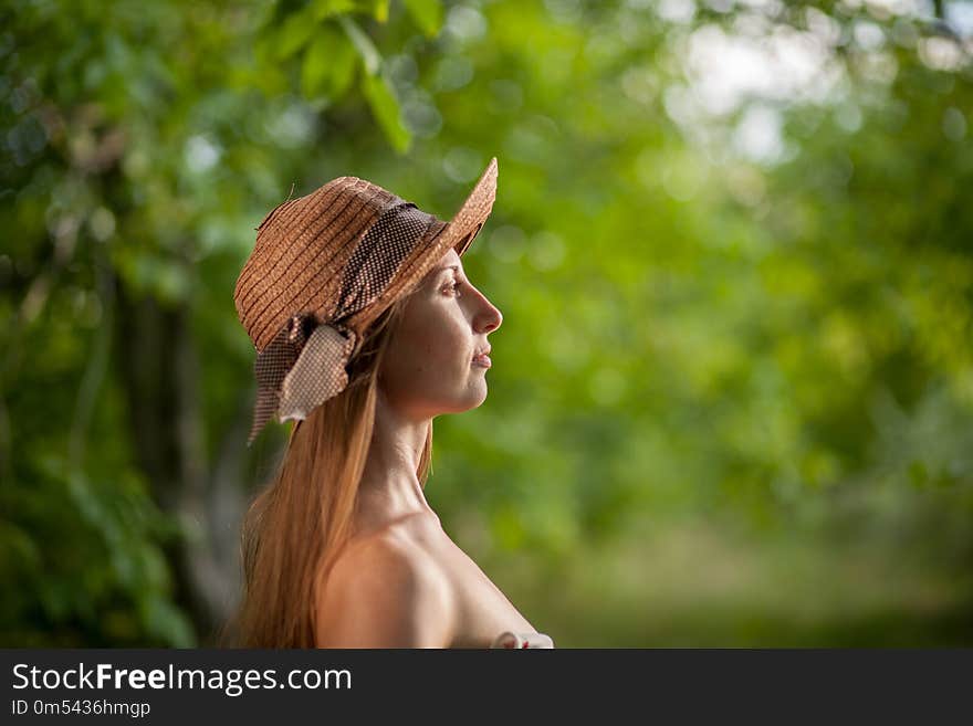 Portrait of a beautiful elegant woman in light white dress and hat standing in the summer park.