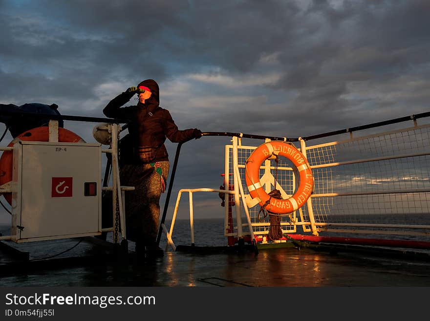 A girl on a ship looks through binoculars at sunset.