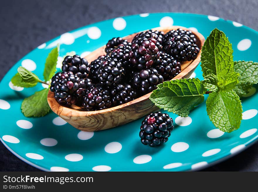 Ripe blackberries with leaves of mint in a bowl on a wooden boar