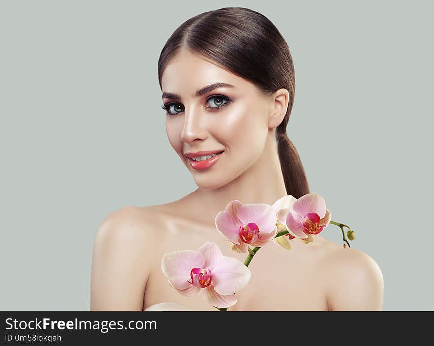 Cute smiling woman with healthy skin and pink orchid flowers. Facial treatment, cosmetology, beauty salon, skin care and spa concept