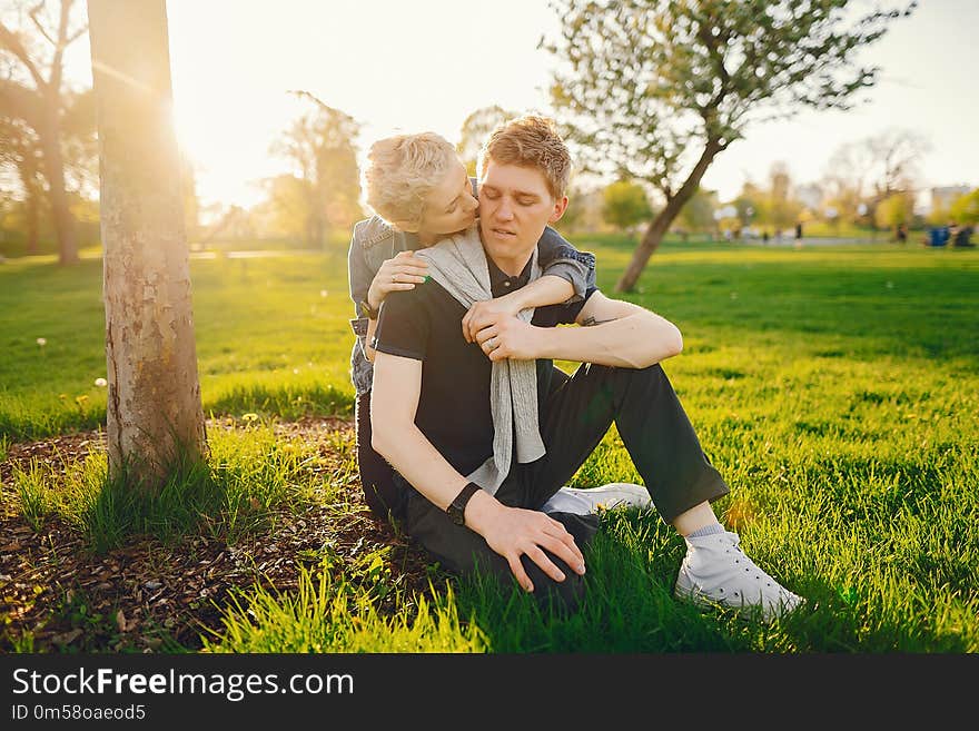 Stylish and beautiful women with short light hair, dressed in a blue jeans jacket sitting with her handsome men in a sunny green park. Stylish and beautiful women with short light hair, dressed in a blue jeans jacket sitting with her handsome men in a sunny green park