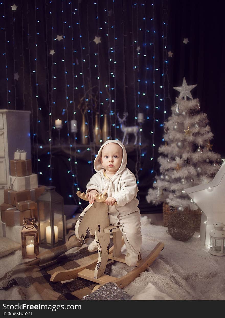 A little boy in a white jumpsuit sitting on a white toy moose. The concept of Christmas. A little boy in a white jumpsuit sitting on a white toy moose. The concept of Christmas