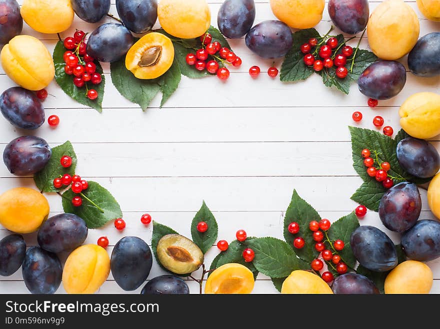 Fresh plum, apricot and red currant berries with leaves on a light table.