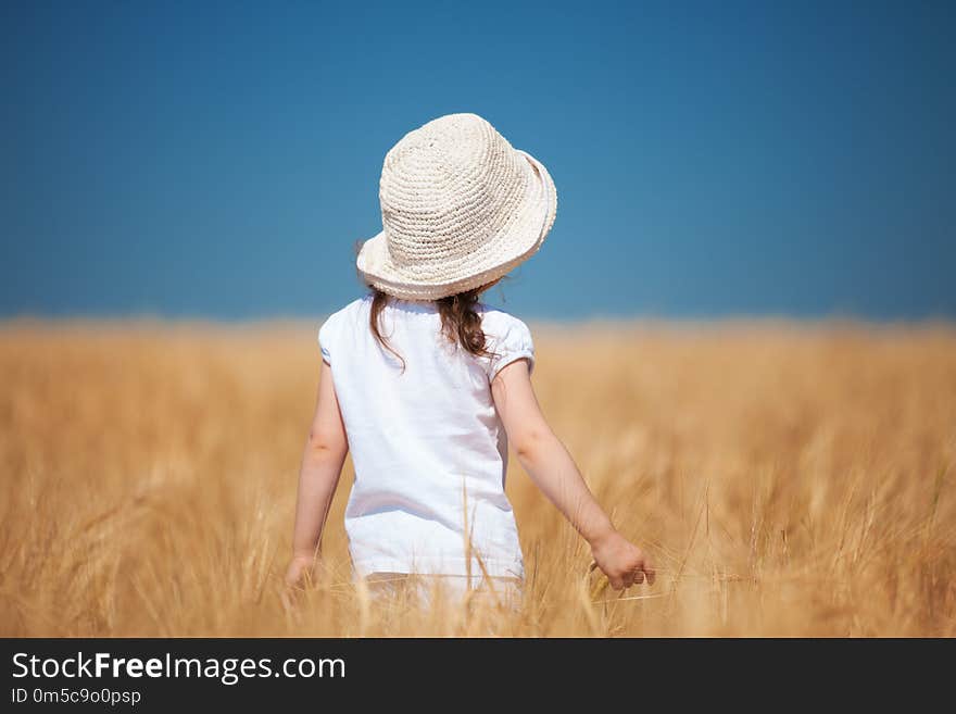 Happy girl walking in golden wheat, enjoying the life in the field. Nature beauty, blue sky and field of wheat. Family outdoor lifestyle. Freedom concept. Cute little girl in summer field