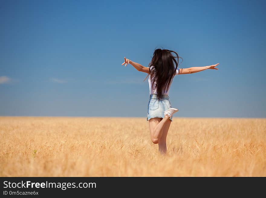 Happy woman enjoying the life in the field Nature beauty, blue sky and field with golden wheat. Outdoor lifestyle. Freedom concept. Woman jump in summer field