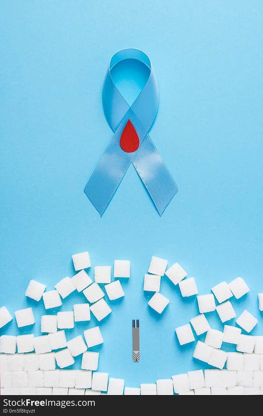 The blue ribbon awareness with red blood drop and wall made of white sugar cubes ruined by Blood Glucose Test Strips on a blue background, world diabetes day. The blue ribbon awareness with red blood drop and wall made of white sugar cubes ruined by Blood Glucose Test Strips on a blue background, world diabetes day