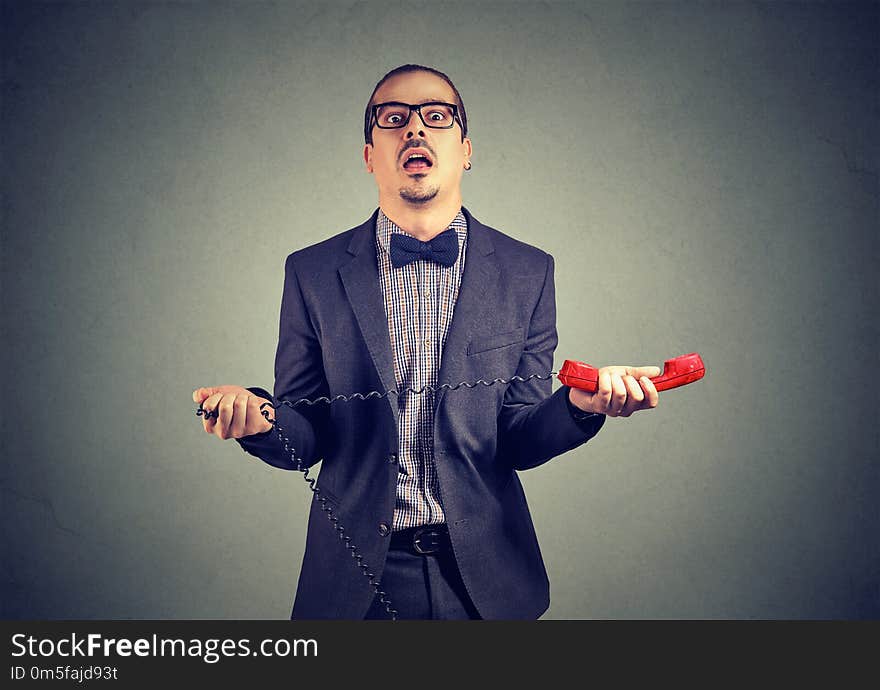 Adult frustrated businessman in suit holding red telephone receiver on gray background. Adult frustrated businessman in suit holding red telephone receiver on gray background