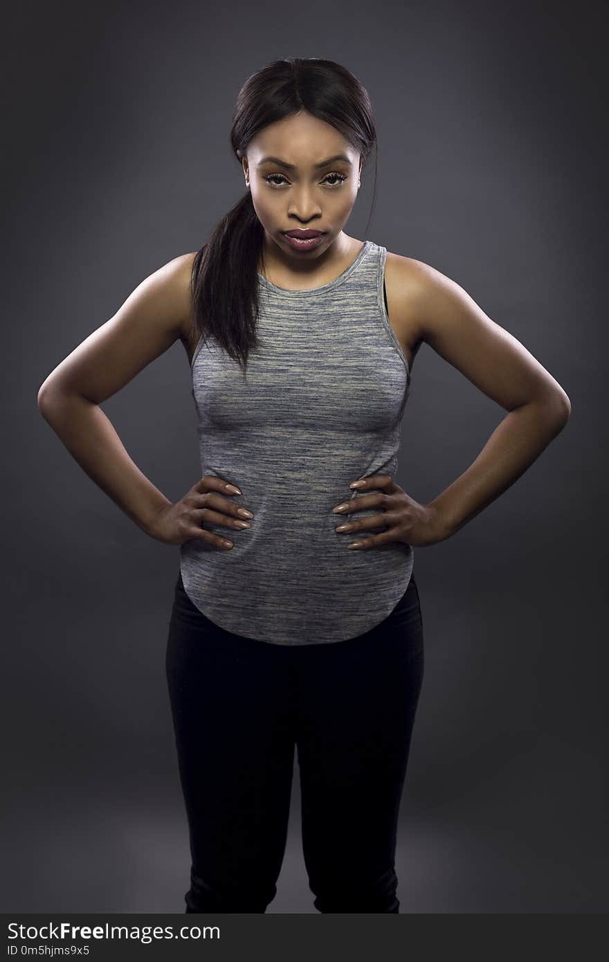 Black fitness trainer or athlete posing as a gritty woman on a dark background. She is fit and slim. The image depicts female sports and health. Black fitness trainer or athlete posing as a gritty woman on a dark background. She is fit and slim. The image depicts female sports and health.