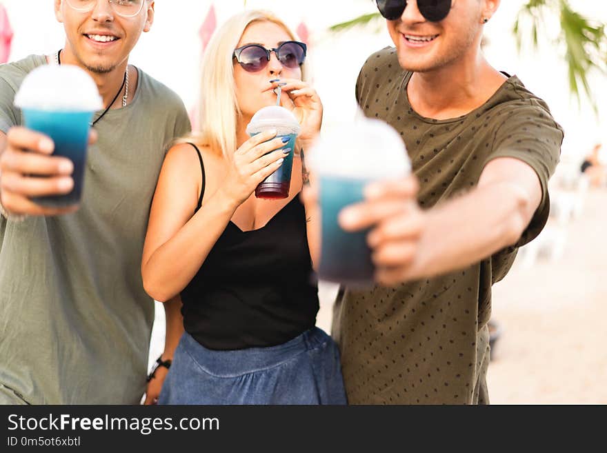 three friends cheerful company rest on a tropical beach and drink cocktails, very, magazine concept