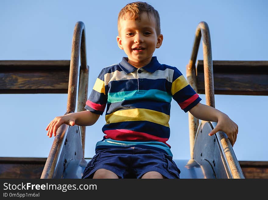 Summer, childhood, leisure, friendship and people concept - happy little boy on children playground slid from the hill