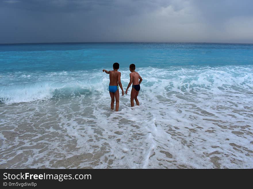 Two boys in the sea watched the waves. Waves and sea and children.