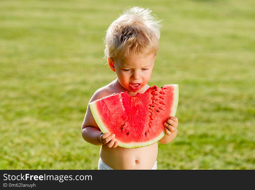 Portrait of toddler child outdoors. Rural scene with one year old baby boy eating watermelon slice in the garden. Dirty messy face of happy kid. Portrait of toddler child outdoors. Rural scene with one year old baby boy eating watermelon slice in the garden. Dirty messy face of happy kid.