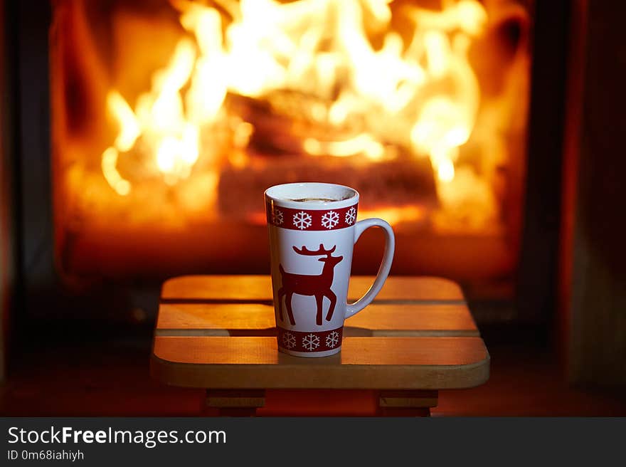 Cup of hot chocolate and marshmallows near fireplace with many candles. Cozy romantic Christmas evening