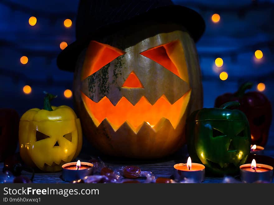 Close up photo of spoofy face of jack-o-lantern, peppers with scary faces, candlelight, bokeh effect, candies