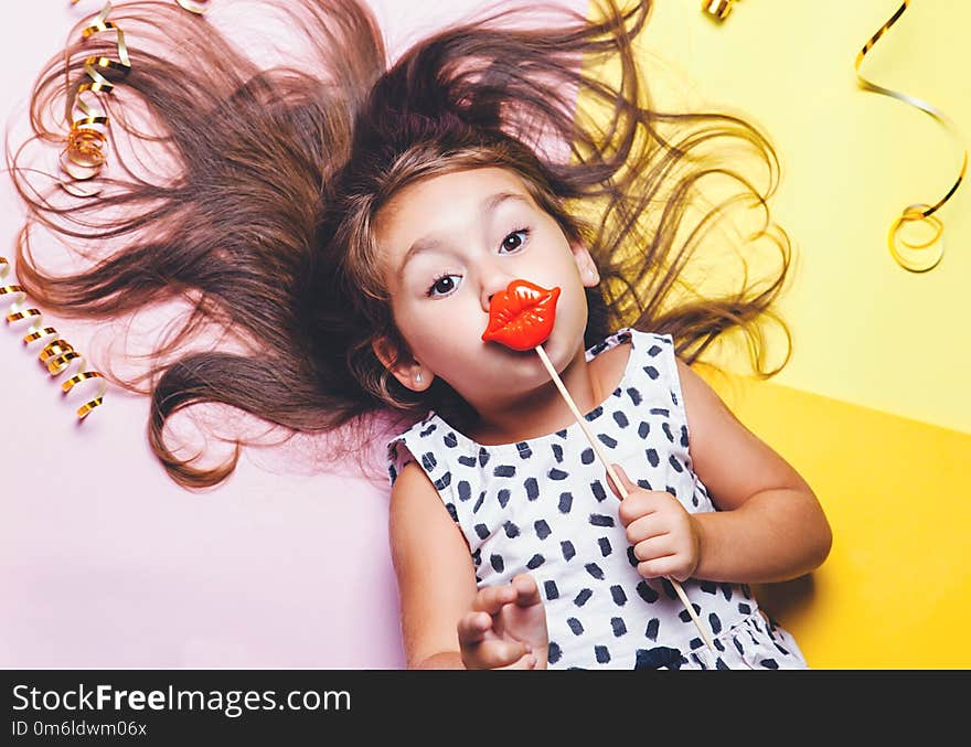 Cute little girl in funny glasses with plastic masquerade lips on stick.. Bright and festive background. Celebration masquerade portrait