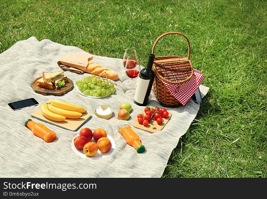 Wicker basket and food on blanket in park. Summer picnic