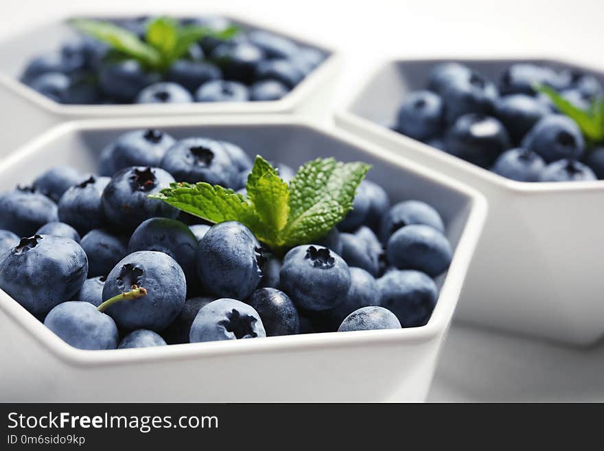 Fresh blueberries with green leaves in white dishware, closeup