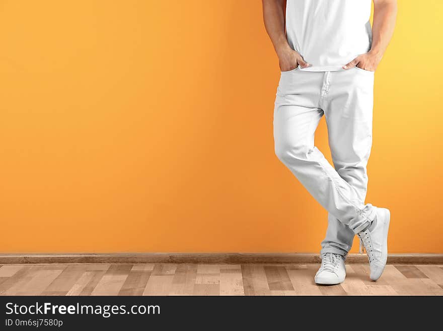 Young man in stylish jeans near color wall with space for text, focus on legs