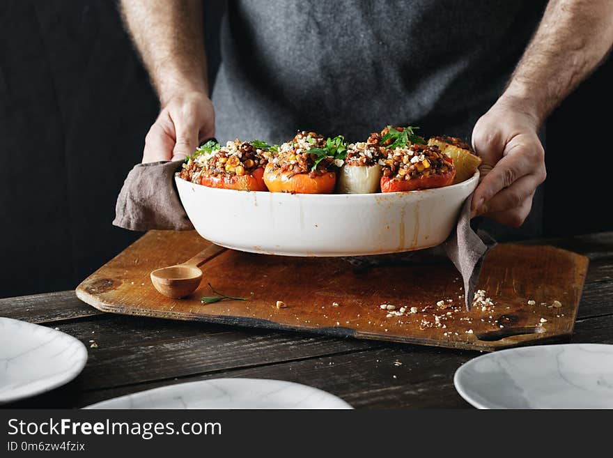 Male hands holding baking dish with cooked stuffed peppers with green lentils, sweet corn, salsa and almonds on wooden table copy space. Healthy, vegetarian food concept. Male hands holding baking dish with cooked stuffed peppers with green lentils, sweet corn, salsa and almonds on wooden table copy space. Healthy, vegetarian food concept