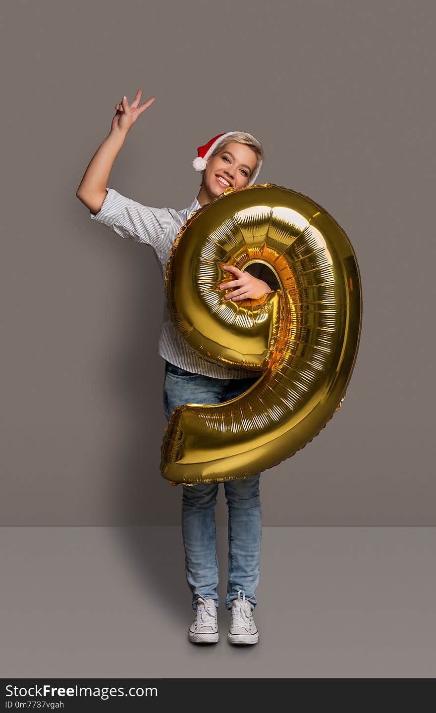 Happy girl with number 9 balloon portrait. Smiling young woman in santa hat at studio background. One of shots to compose 2018 for new year and christmas greeting card