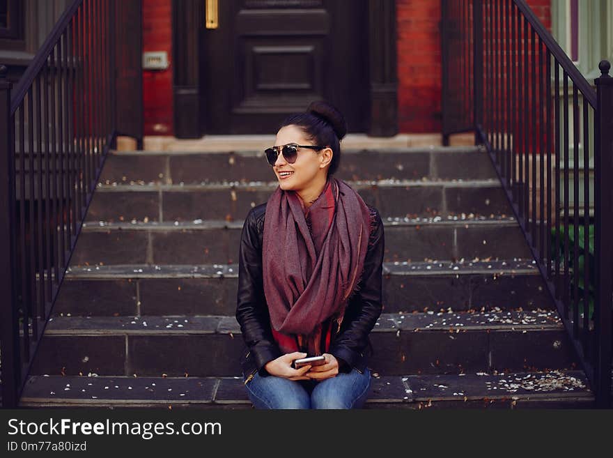 Beautiful young girl in a leather jacket and scarf sitting on the stairs and use the phone