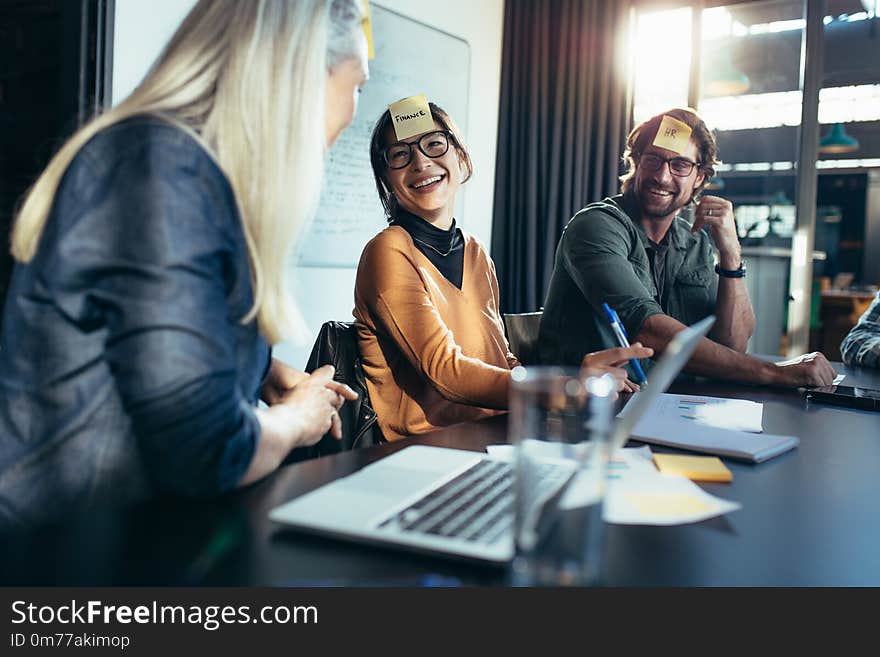 Smiling asian women with sticky note on her forehead sitting with colleagues in meeting. Diverse business team having a brainstorming meeting in board room. Smiling asian women with sticky note on her forehead sitting with colleagues in meeting. Diverse business team having a brainstorming meeting in board room.