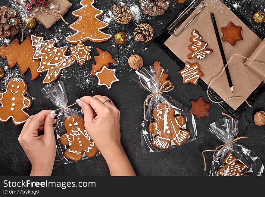 Christmas gift gingerbread on dark background. Christmas Gingerbread Cookies. Biscuits in festive packaging. Woman is packaging Christmas gingerbread cookies with icing sugar. Holiday, celebration and cooking concept. Christmas preparations concept. Top view. Christmas gift gingerbread on dark background. Christmas Gingerbread Cookies. Biscuits in festive packaging. Woman is packaging Christmas gingerbread cookies with icing sugar. Holiday, celebration and cooking concept. Christmas preparations concept. Top view