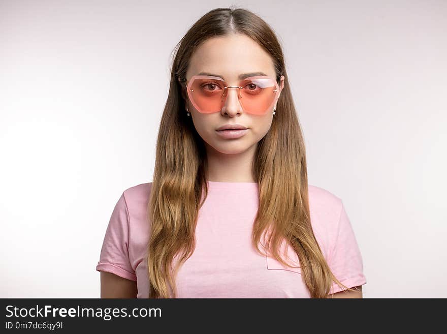 Stylish fair-haired woman looking through pink sunglasses to the camera