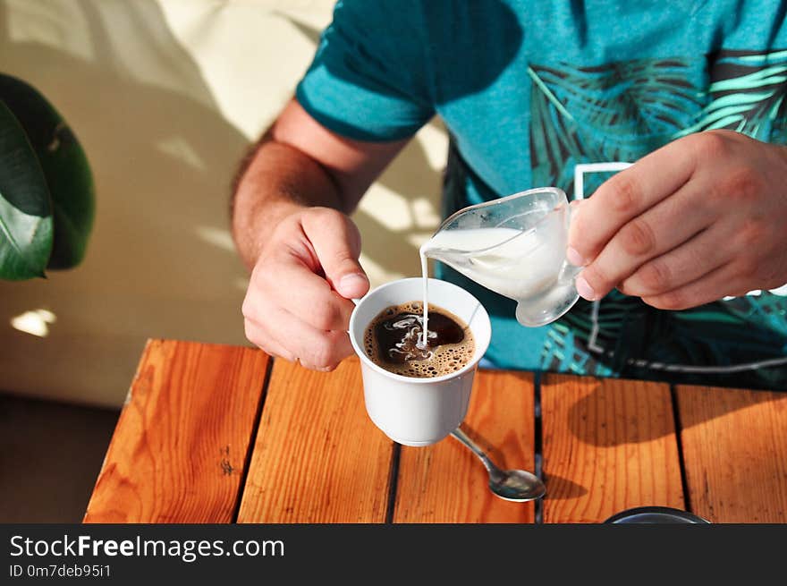 A man in a cafe pours cream into a Cup of coffee in the morning. Breakfast.