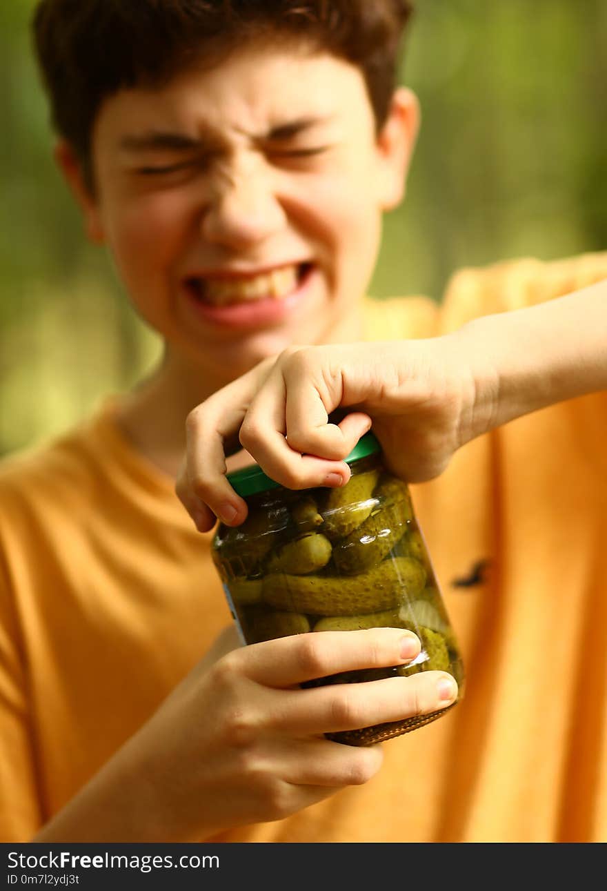 Boy with strain grimace try to remove cover from cucumbers jar