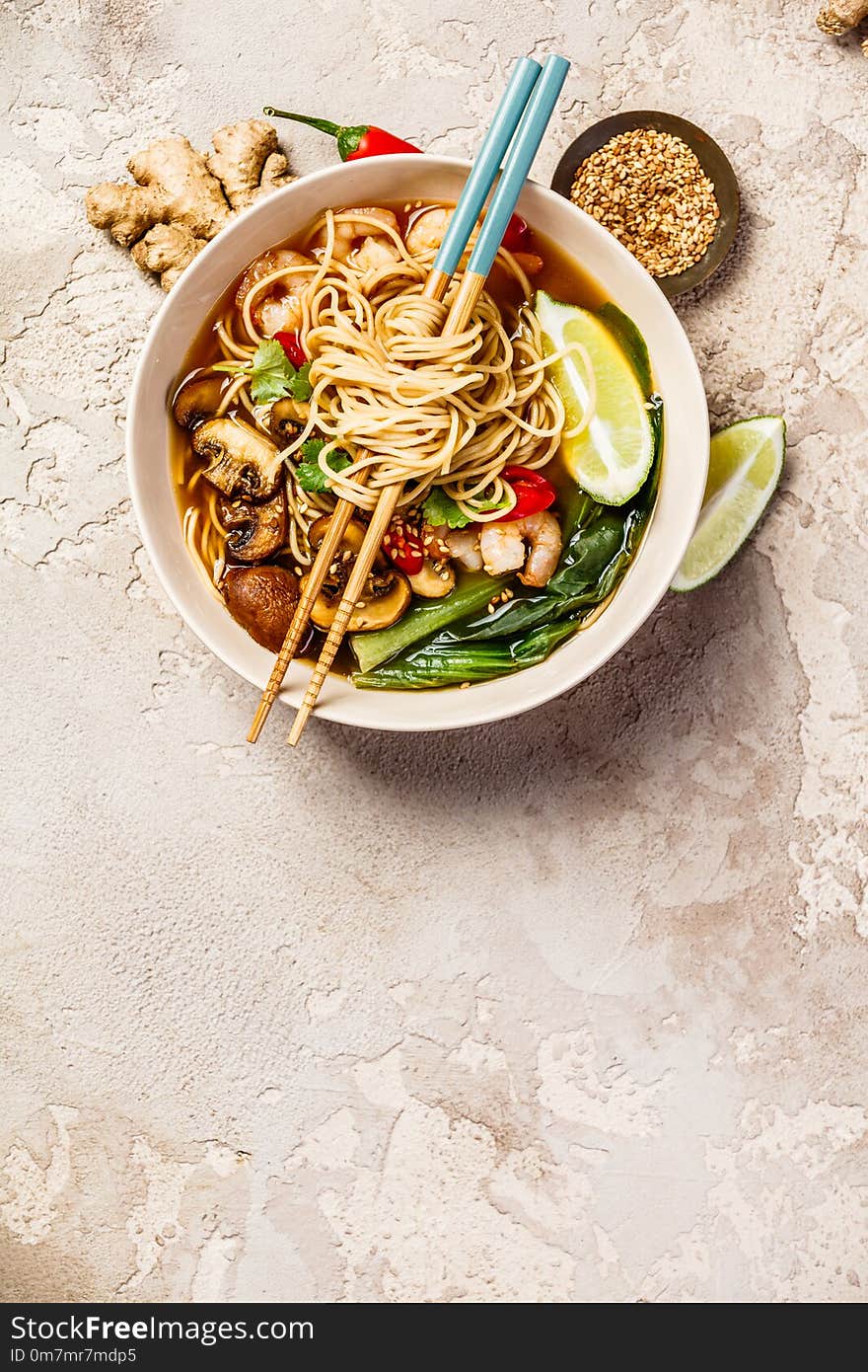 Asian soup with noodles ramen, with miso paste, soy sauce, greens, mushrooms and shrimps prawn. On a stone table, with chopsticks, ginger and lime