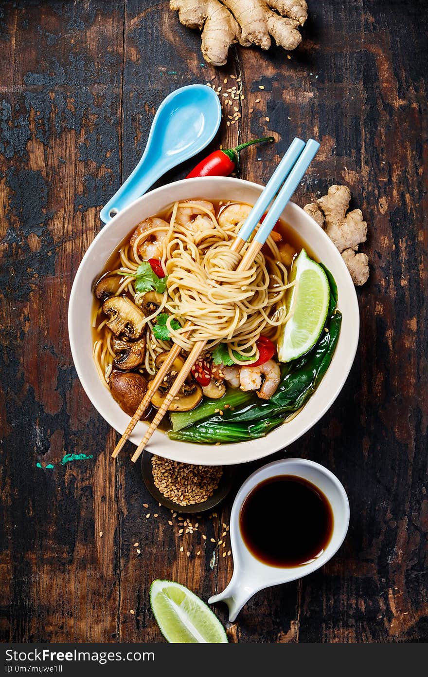 Asian soup with noodles ramen, with miso paste, soy sauce, greens, mushrooms and shrimps prawn. On wooden table, with chopsticks.