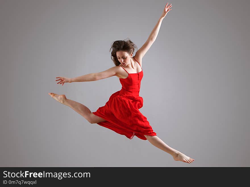 Portrait of elegant dancer in red dress jumping against gray background