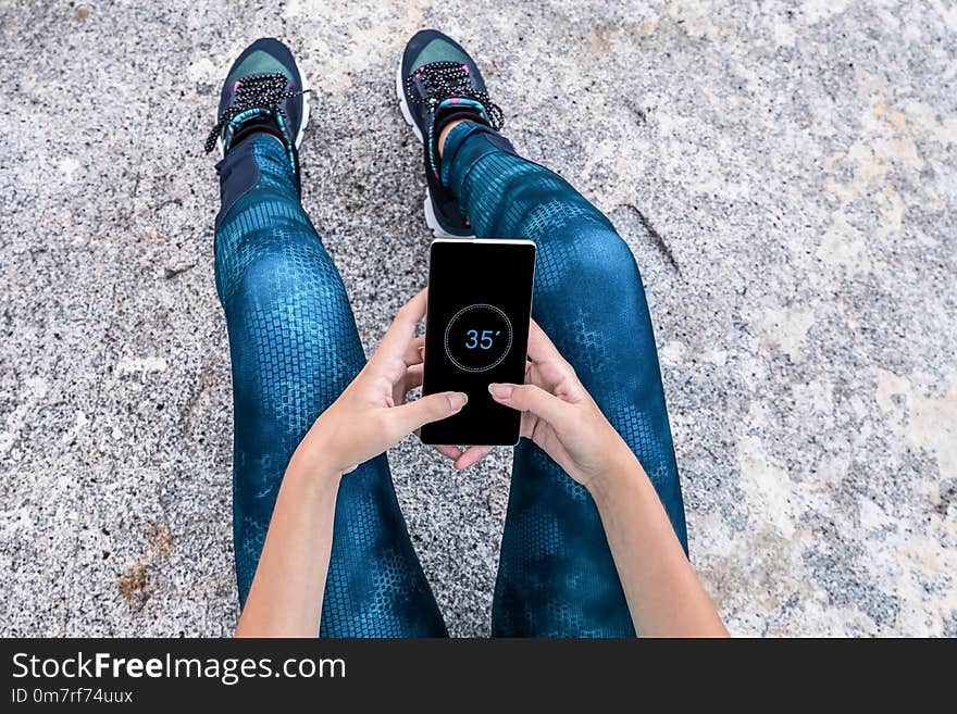 Young woman watching her smartphone on a rock. Tired on a rock, resting her time watching her phone.