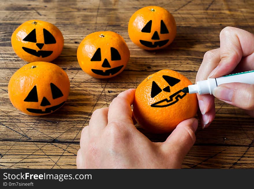 Hands Draw A Face On A Tangerine On Halloween