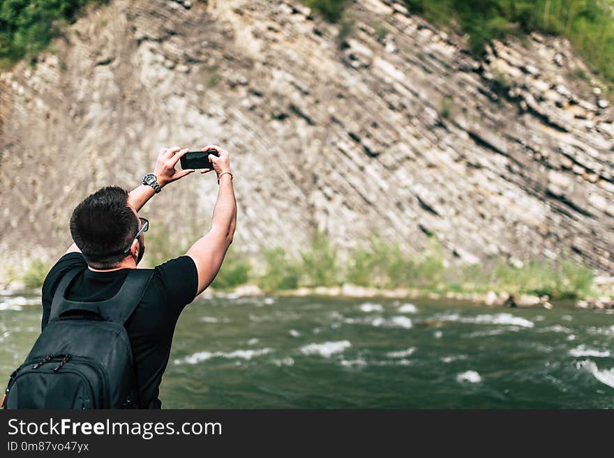 Traveler with backpack making photo on mobile phone near mountain river. Traveler with backpack making photo on mobile phone near mountain river