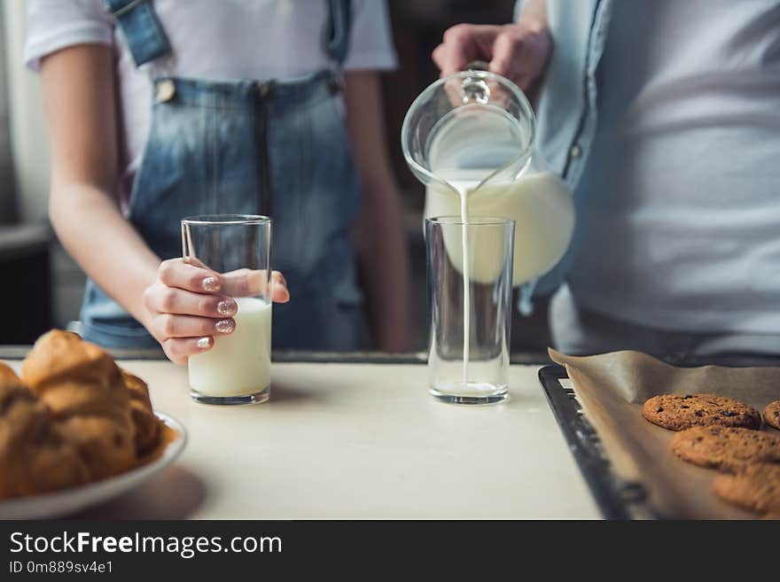 Cropped image of mom and daughter in casual clothes in kitchen at home, mom is pouring milk