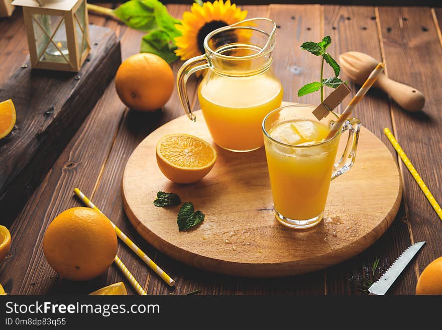 Glass of fresh pressed orange juice with ice cubes and oranges on wooden table. Autumn cozy rustic mood still life